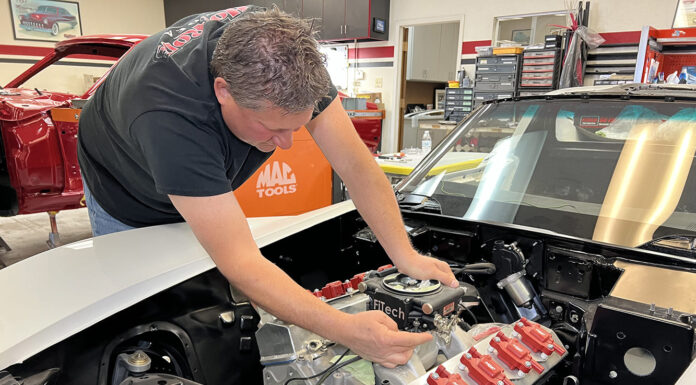 Mechanic lowering and test-fitting a FiTech Go EFI 4 throttle body onto an intake manifold in a 1971 Corvette engine bay.