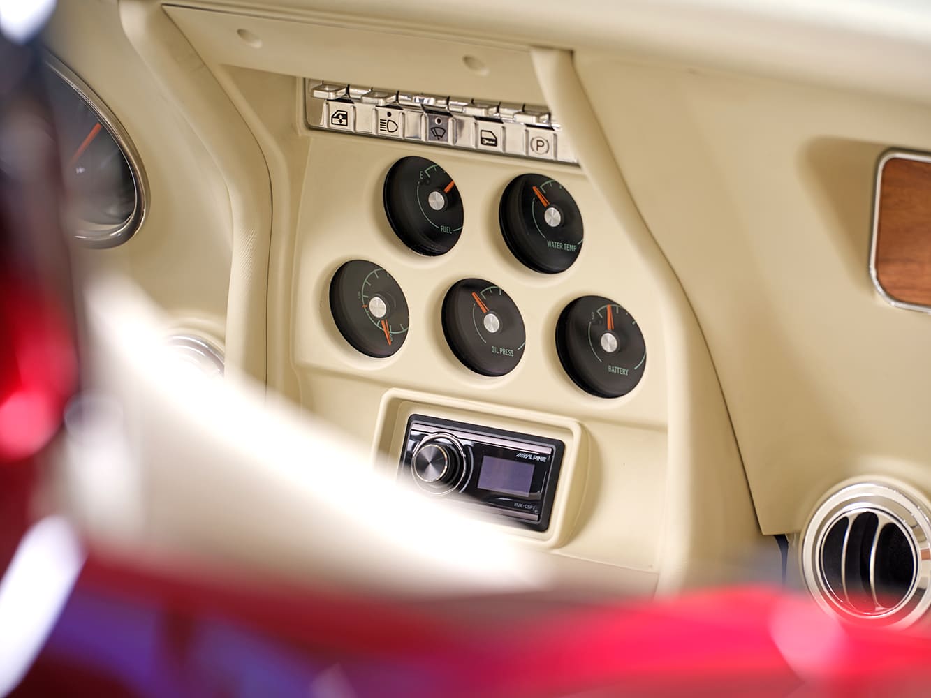Close-up of the cream-finished center dash console housing five black-face analog gauges, indicator lights, and an Alpine stereo head unit.