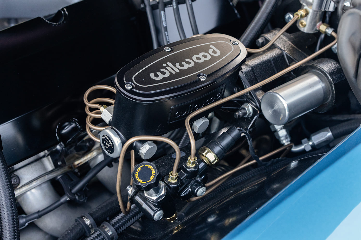 Detailed view of a black Wilwood aluminum master cylinder, hard brake lines, and adjustable proportioning valve mounted on the inner fender of the 1966 Chevelle.