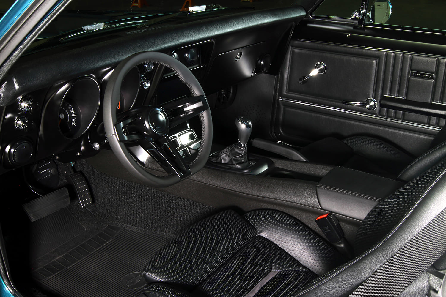 Interior view of a 1967 Camaro featuring black leather sport bucket seats, modern center console, shifter, and aftermarket steering wheel.