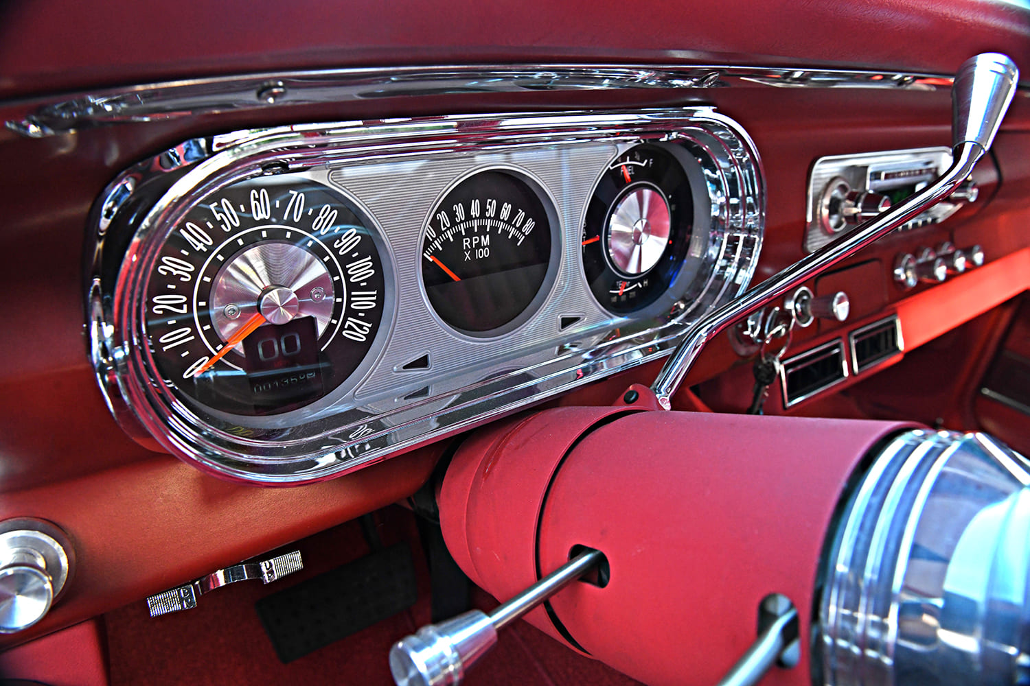 Close-up of a billet aluminum gauge cluster featuring analog-style dials and digital readouts integrated into the painted red dashboard of a 1962 Chevy Nova.
