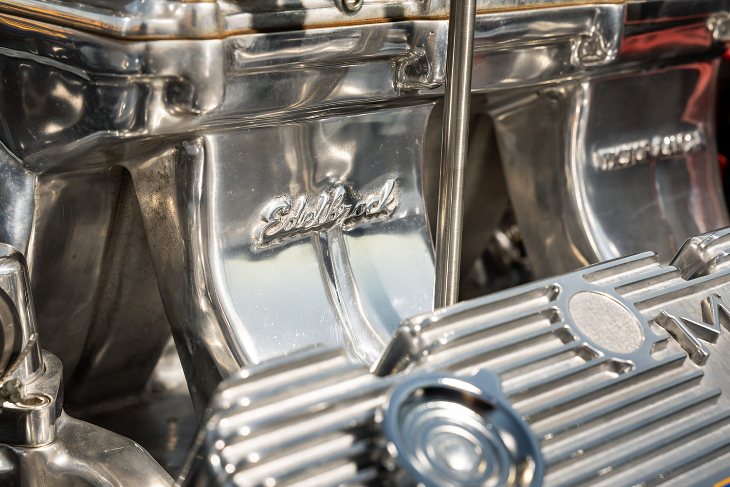Close-up of the polished aluminum Edelbrock Victor Ram intake manifold runner next to a finned valve cover.