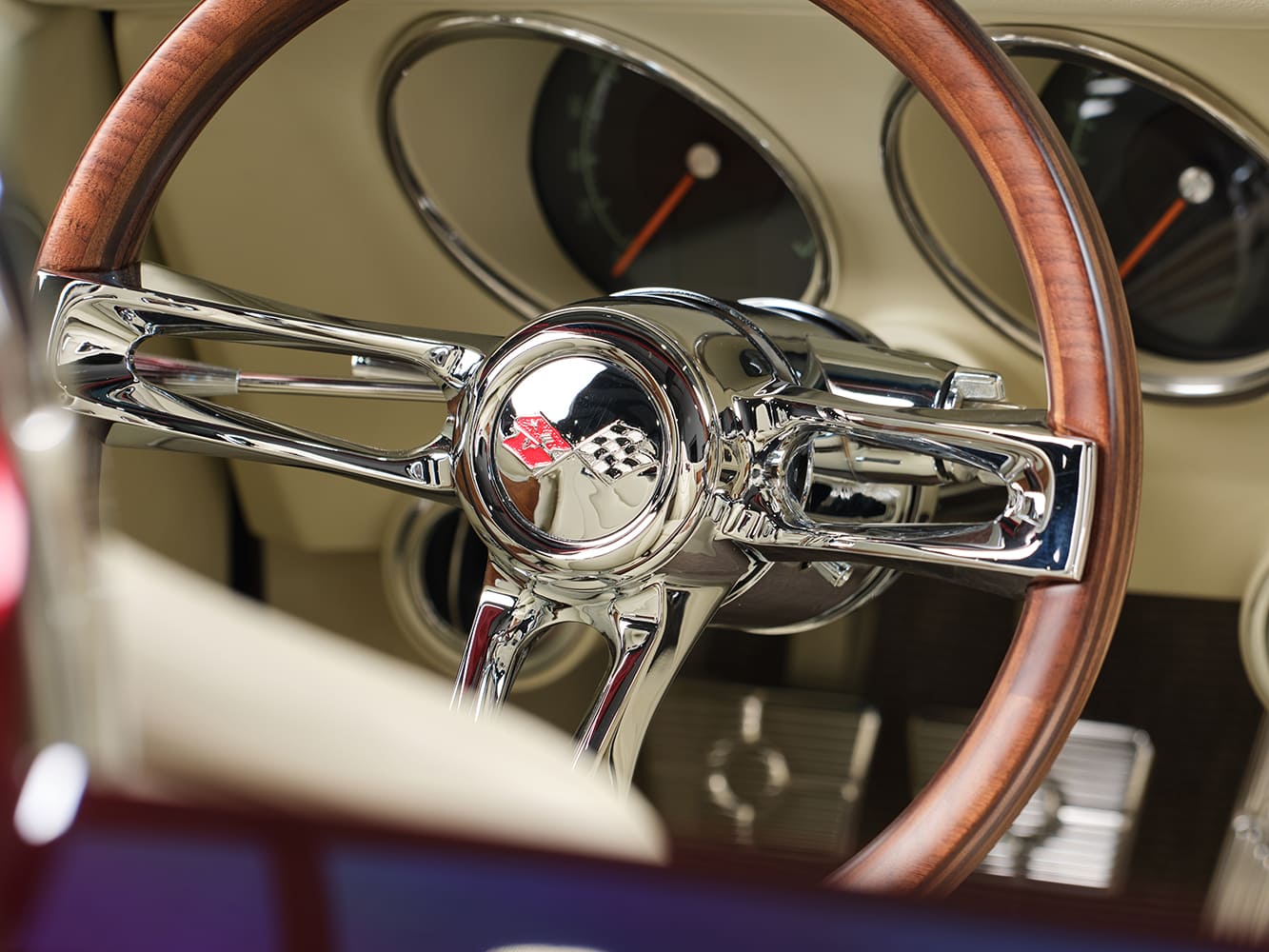 Close-up of the polished billet three-spoke steering wheel with a wood outer rim and chrome crossed-flags Corvette horn cap.