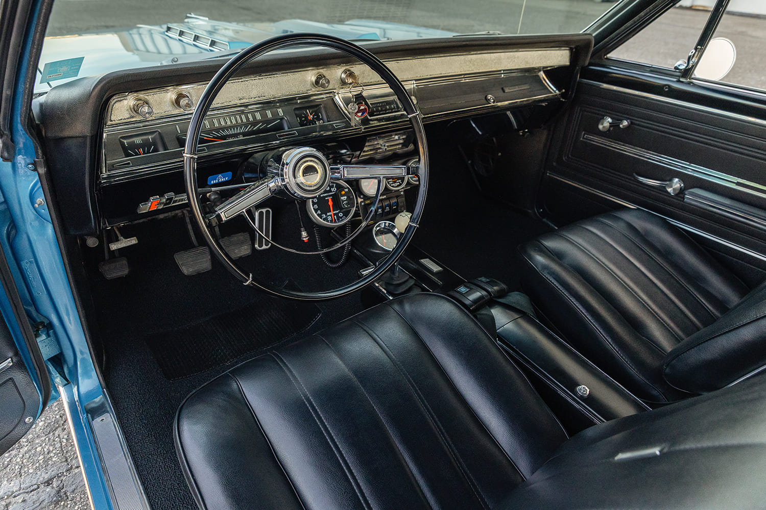 Driver-side cabin view of the Marina Blue 1966 Chevelle SS showing black vinyl bucket seats, four-speed console shifter, and steering-column tachometer.