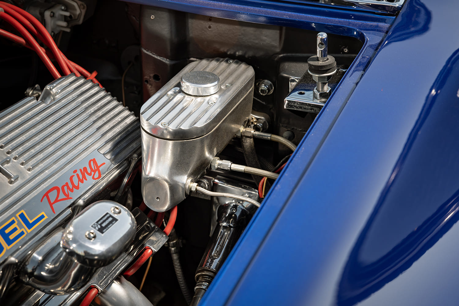Close-up of a polished finned aluminum brake master cylinder reservoir and quick-release hood pin mount in the inner fender bay.