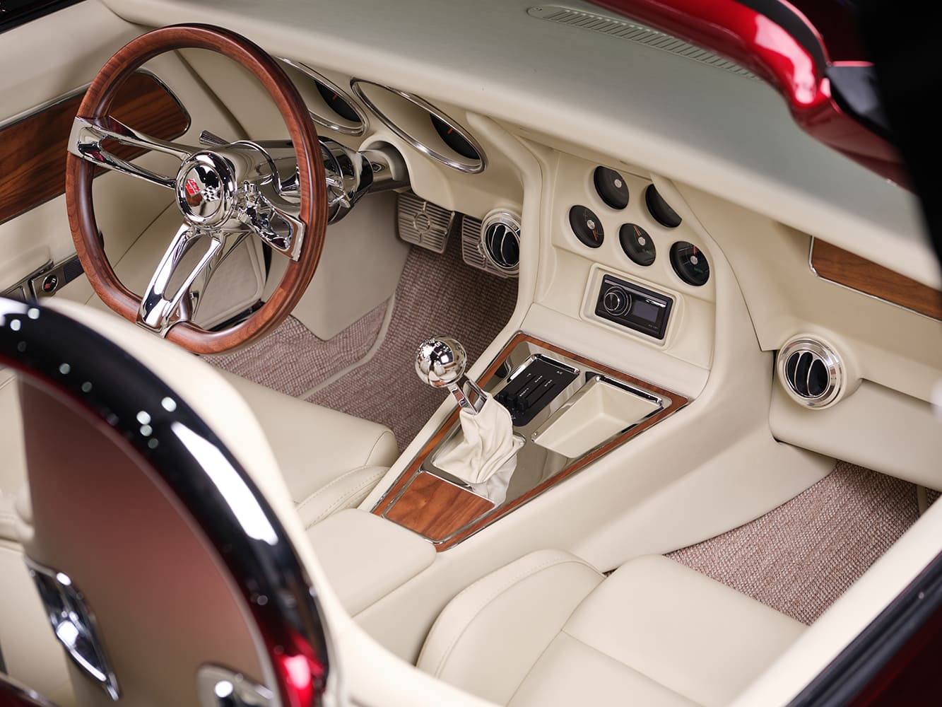 High-angle driver-side cockpit shot featuring cream leather upholstery, woodgrain door inserts, spherical chrome shifter, and center dash gauge console.