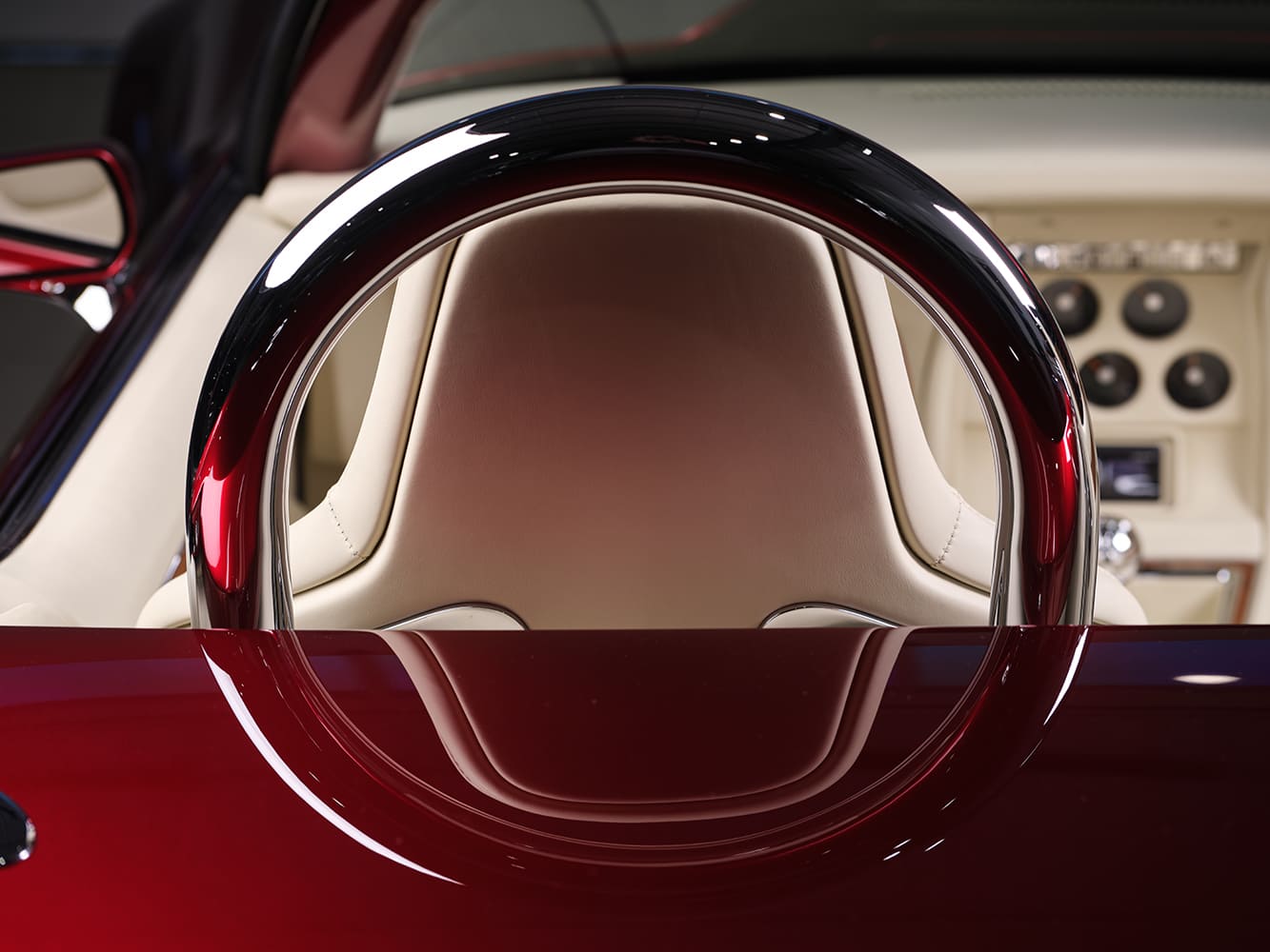 Close-up looking past the polished chrome driver-side roll hoop framing the contoured cream leather headrest and rear deck.