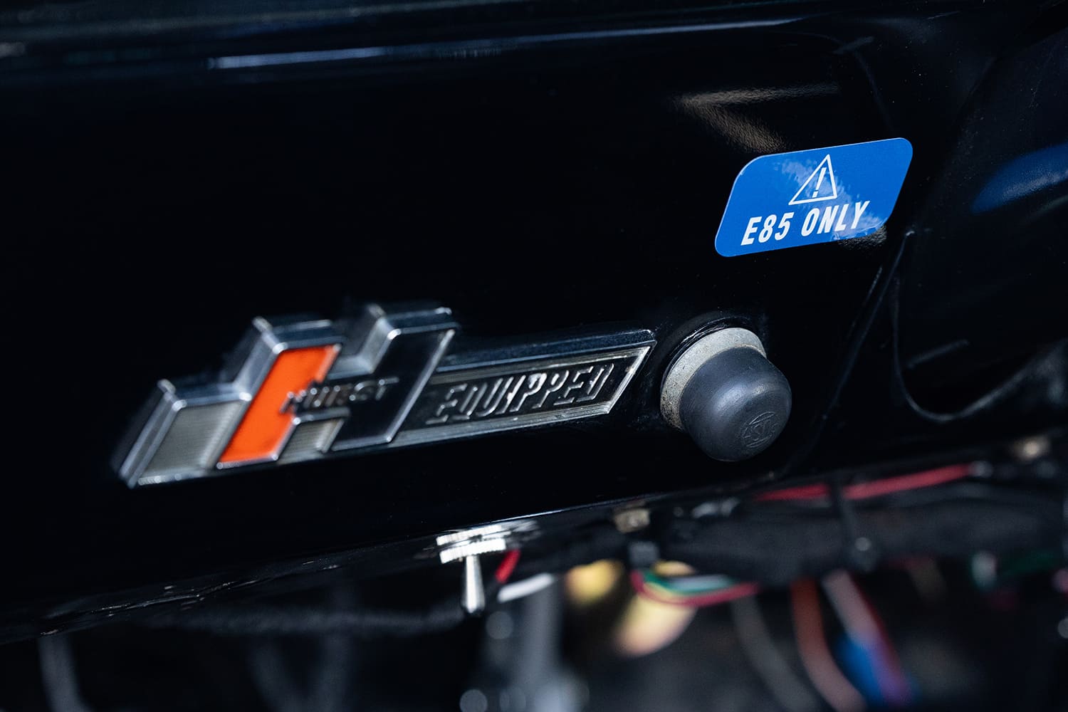 Detail shot of the black dashboard featuring a vintage chrome Hurst Equipped emblem beside a blue warning sticker labeled "E85 ONLY".