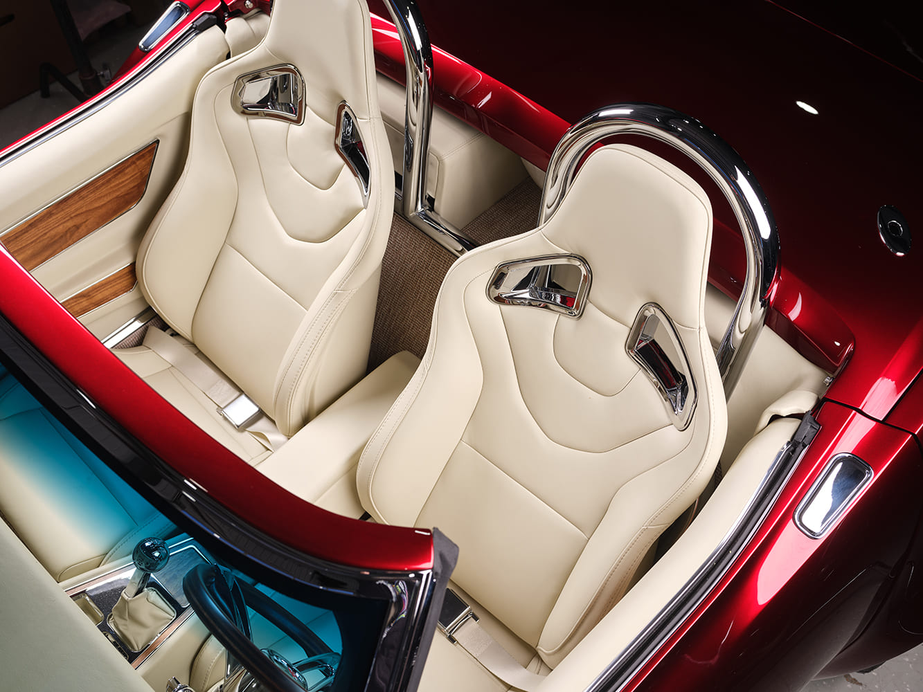Overhead perspective of the open roadster cabin highlighting twin cream high-back bucket seats with chrome harness cutouts and matching roll bars.