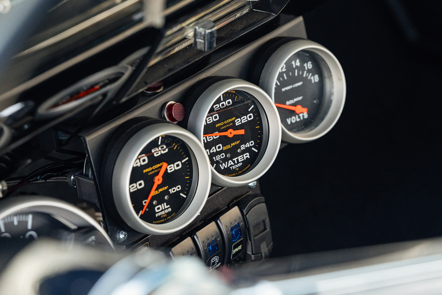 Close-up of three silver-bezel AutoMeter gauges monitoring oil pressure, water temperature, and voltage mounted under the Chevelle dashboard.