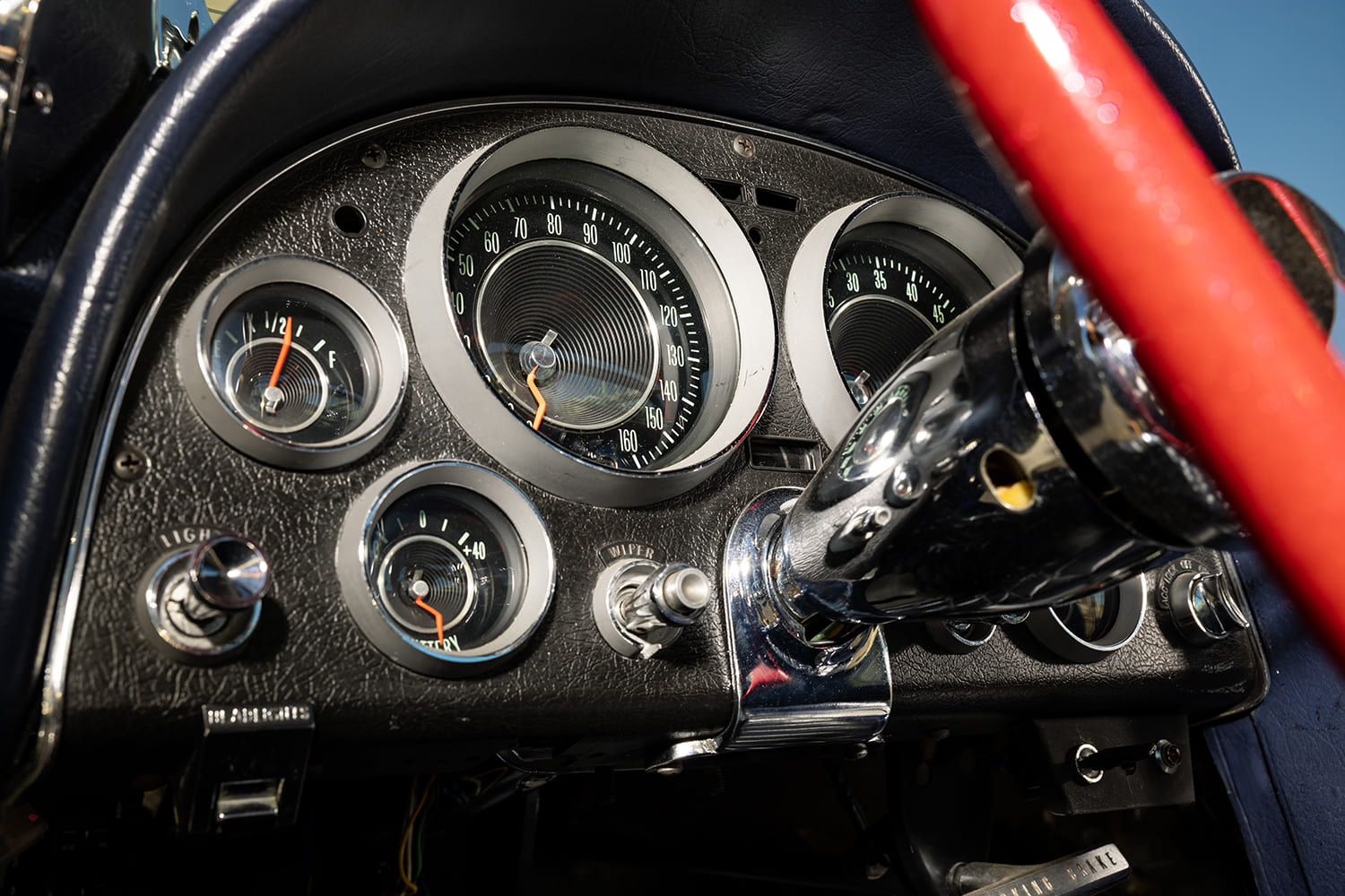 Close-up of the textured black instrument cluster with 160-mph speedometer, factory auxiliary gauges, and chrome steering column.
