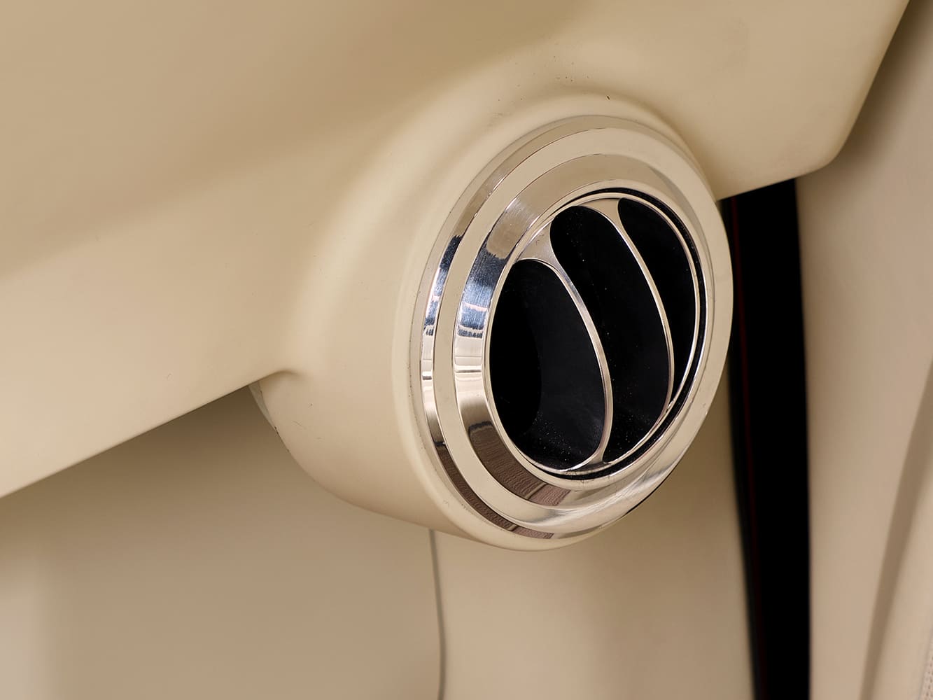 Macro view of a polished billet aluminum circular air conditioning vent bezel integrated into the cream leather-wrapped dashboard.