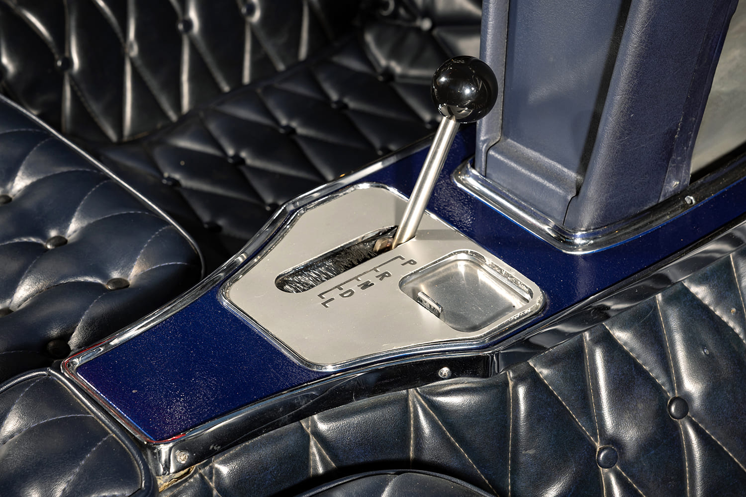 Close-up of the center console automatic floor shifter surrounded by custom dark blue button-tufted upholstery.
