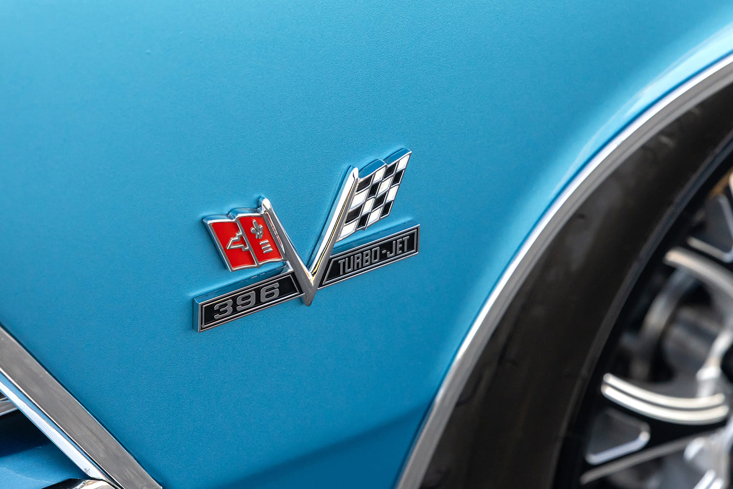 Close-up of the iconic Chevrolet crossed-flags fender emblem with "396 Turbo-Jet" script on the blue paint beside the front wheel opening.