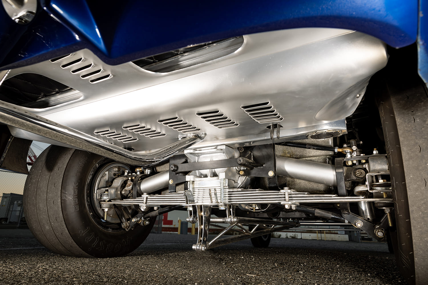 Undercarriage view showing the heavy-duty rear independent suspension, multi-leaf spring, tie rods, and louvered aluminum belly pan.