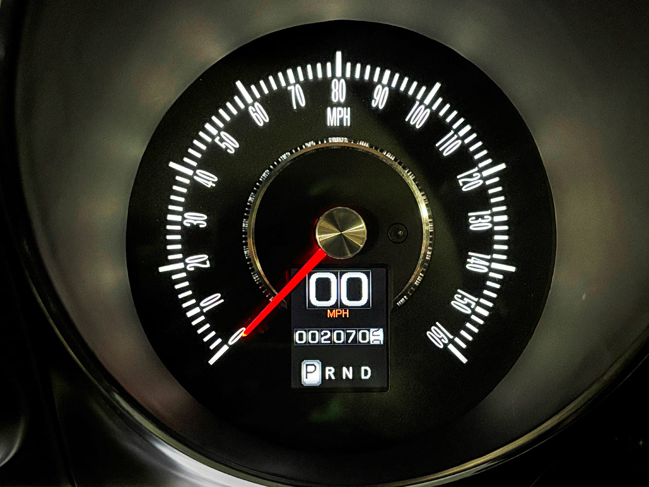 Close-up of a circular electronic 160-mph speedometer featuring an integrated digital speed readout, odometer, and PRND gear selection display.