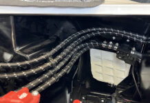Clean routing of four black braided Pure Stealth hoses secured with billet chassis clamps along the gloss black inner fender and firewall.