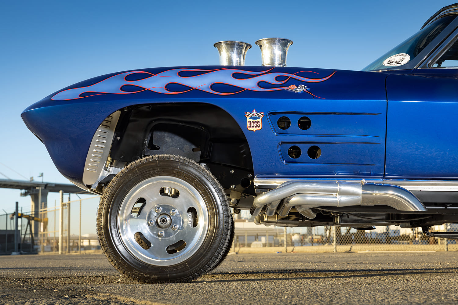 Close-up profile of the front fender flame graphic, Hoss fender badge, polished side-exit headers, and slotted front runner wheel.