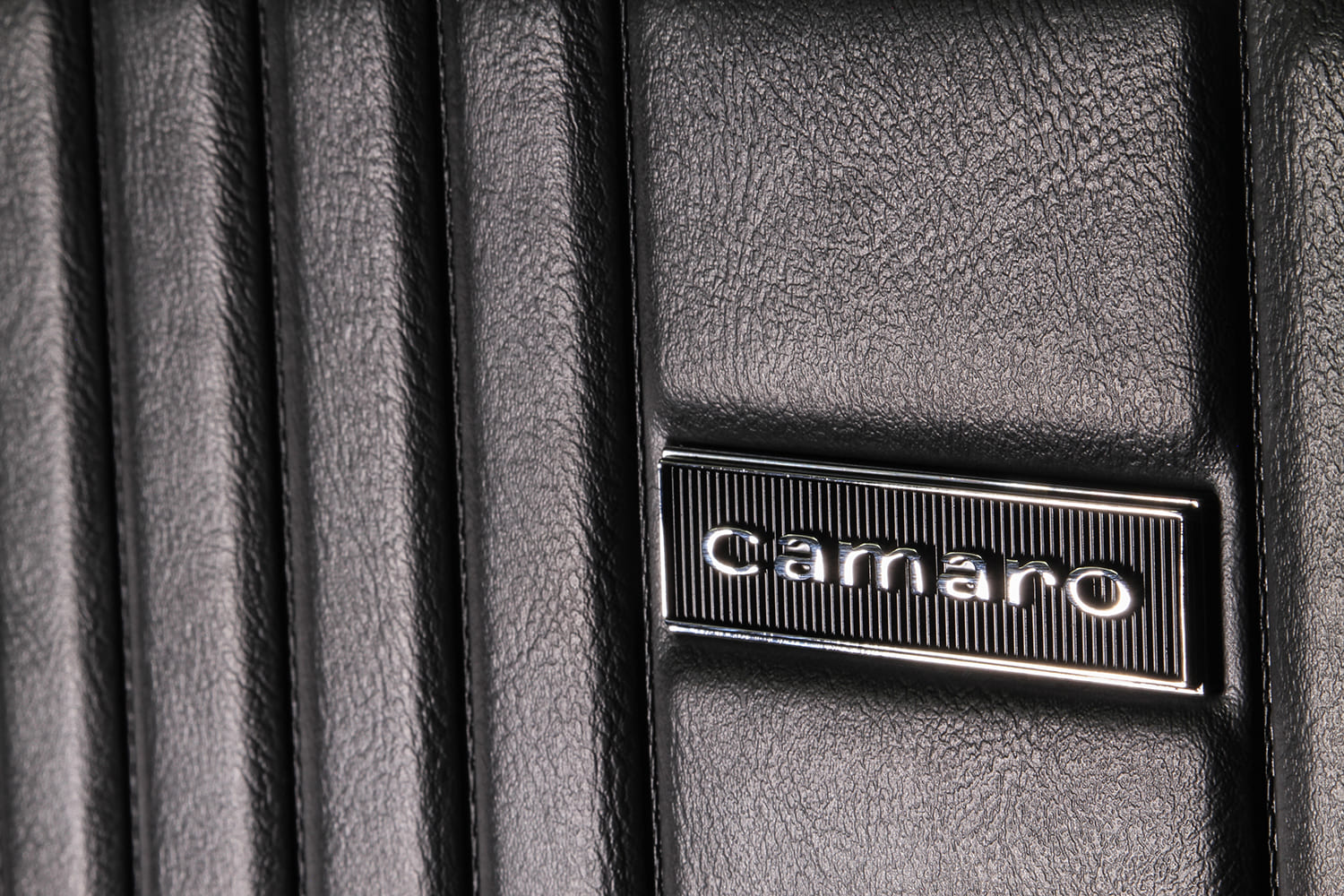 Chrome ribbed Camaro emblem badge mounted on textured black leather interior upholstery.