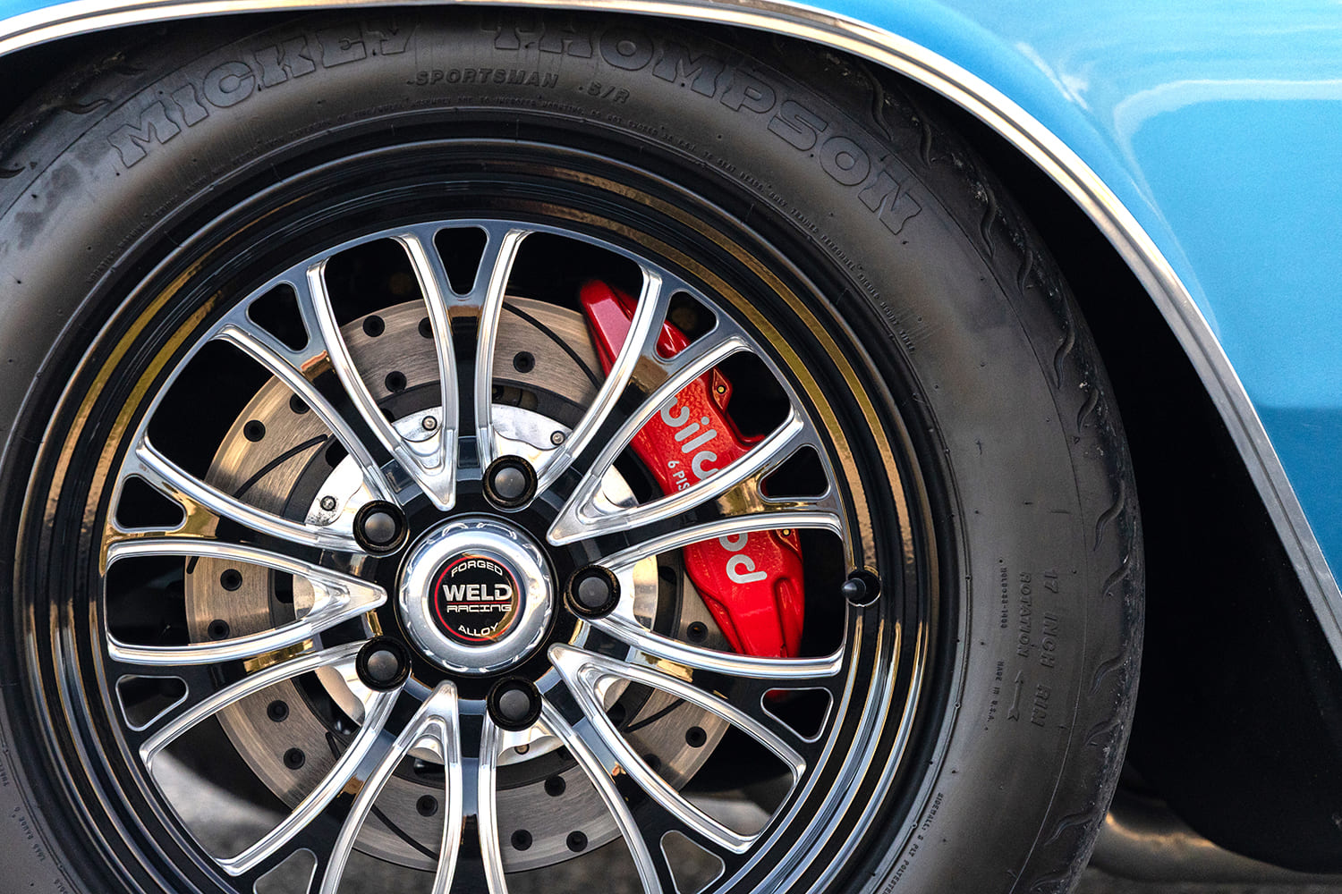 Close-up of a forged Weld Racing front runner wheel wrapped in a Mickey Thompson Sportsman S/R tire, revealing drilled and slotted rotors with a red Wilwood six-piston brake caliper.