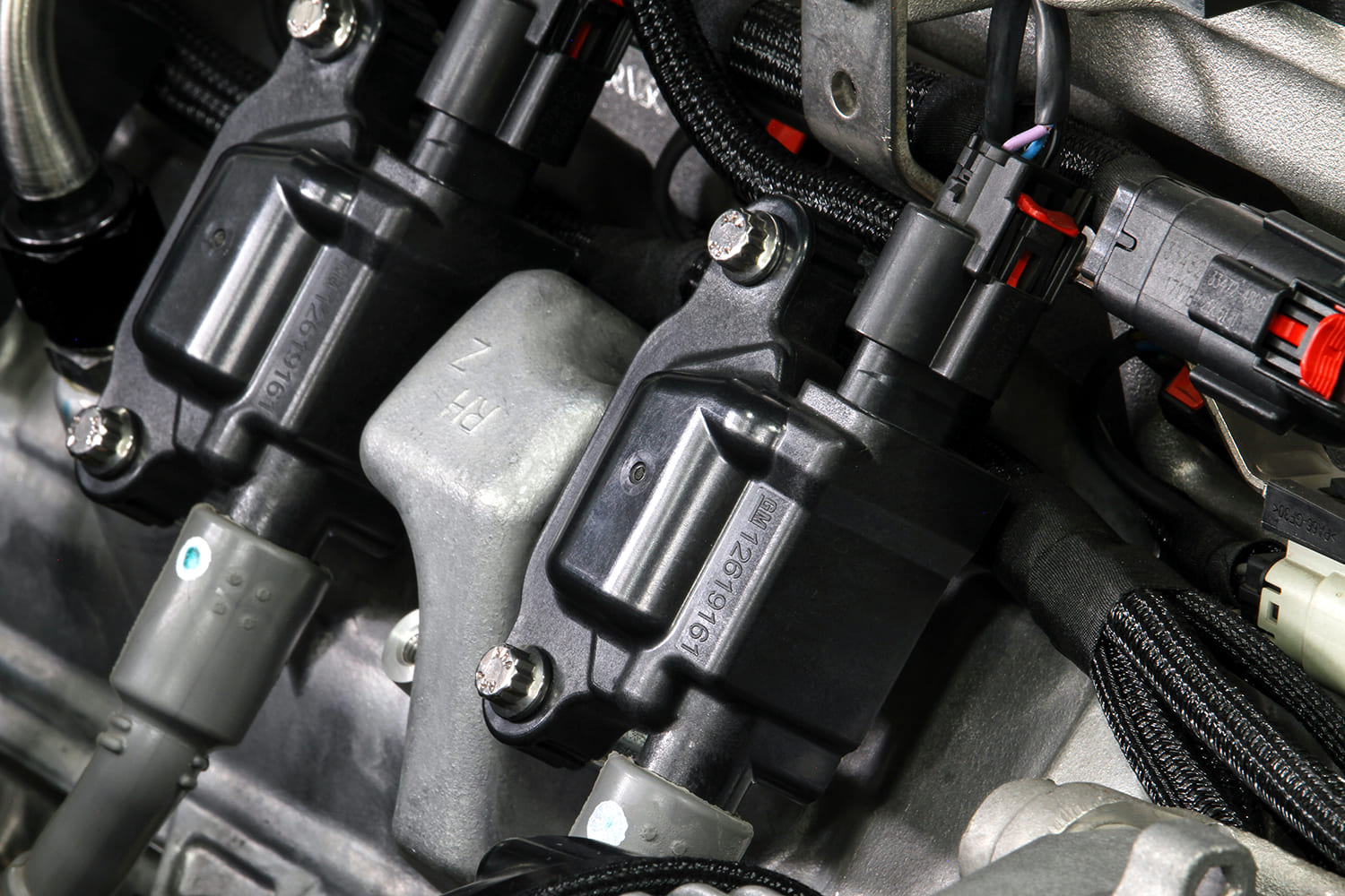 Close-up of GM coil-on-plug ignition coils mounted on the cylinder head with factory connectors and braided wiring loom.