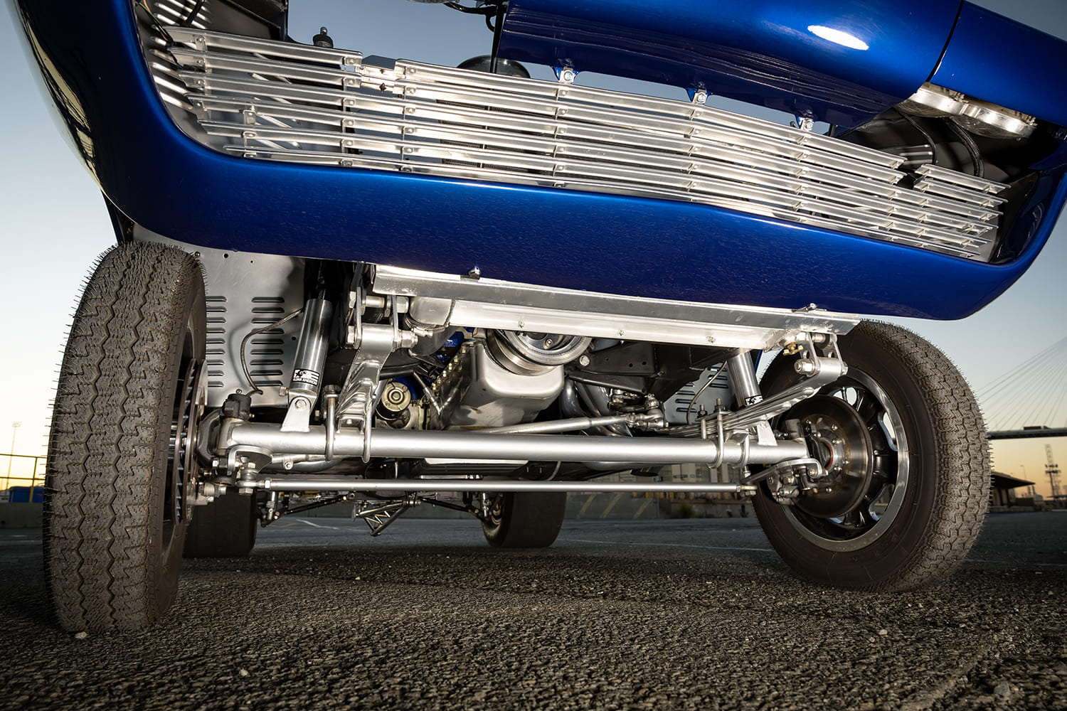 Low ground-level view of the front suspension showcasing the silver straight tube axle, leaf springs, steering rod, and disc brakes.