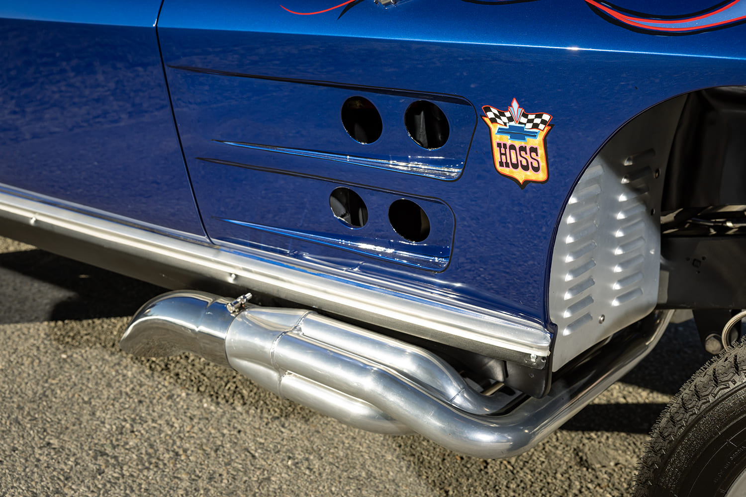 Close-up of the front lower fender featuring drilled cooling ports, Hoss emblem, louvered inner panel, and polished side-dump headers.