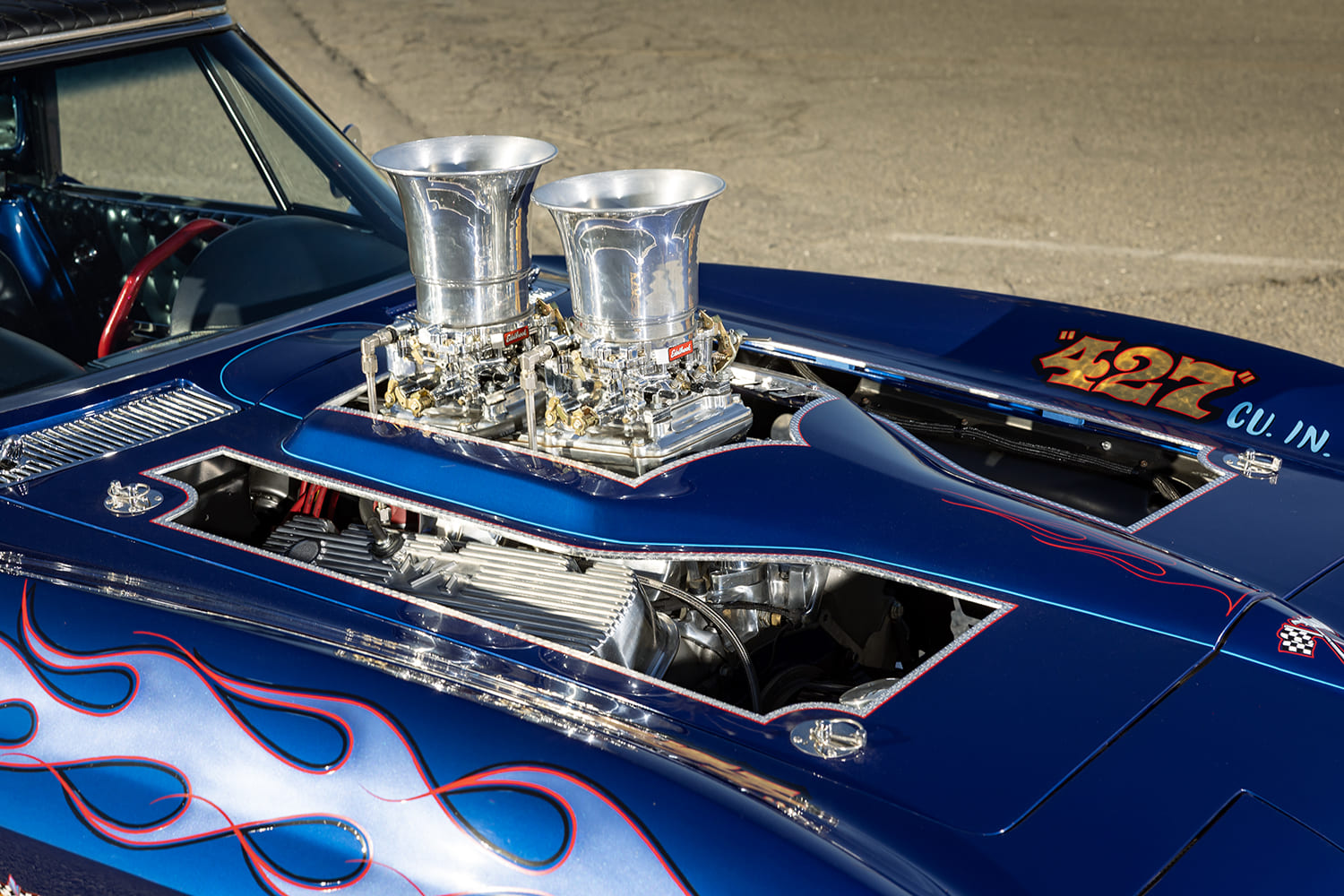 Angle view of the blue painted hood cutout framed with pinstriping, revealing the tunnel ram intake and tall velocity stacks.