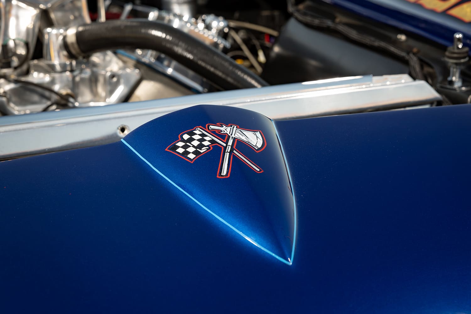 Extreme close-up of the hand-painted crossed battle-axe and checkered flag emblem on the peaked blue fiberglass nose.