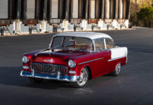 Front three-quarter angle of a lowered 1955 Chevrolet Bel Air sedan highlighting the deep red metallic paint and classic hood bird ornament.
