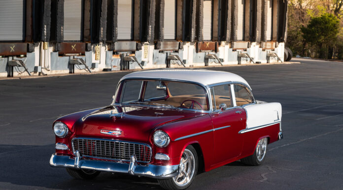 Front three-quarter angle of a lowered 1955 Chevrolet Bel Air sedan highlighting the deep red metallic paint and classic hood bird ornament.