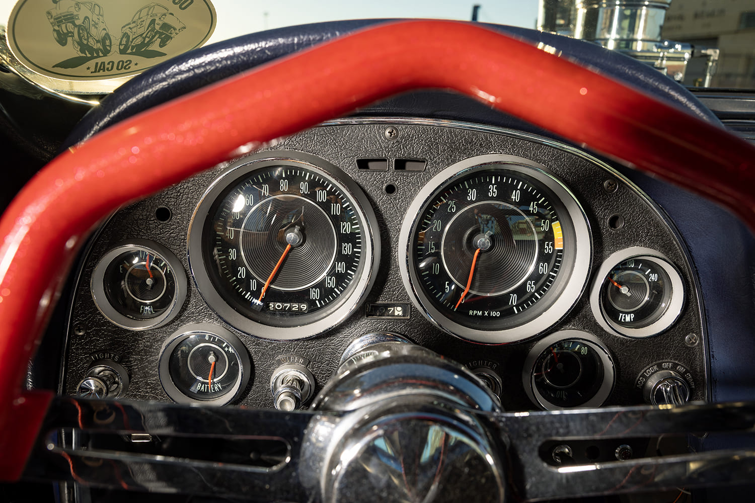 Close-up driver's perspective through a red steering wheel showing the 160-mph speedometer, tachometer, and auxiliary gauges.