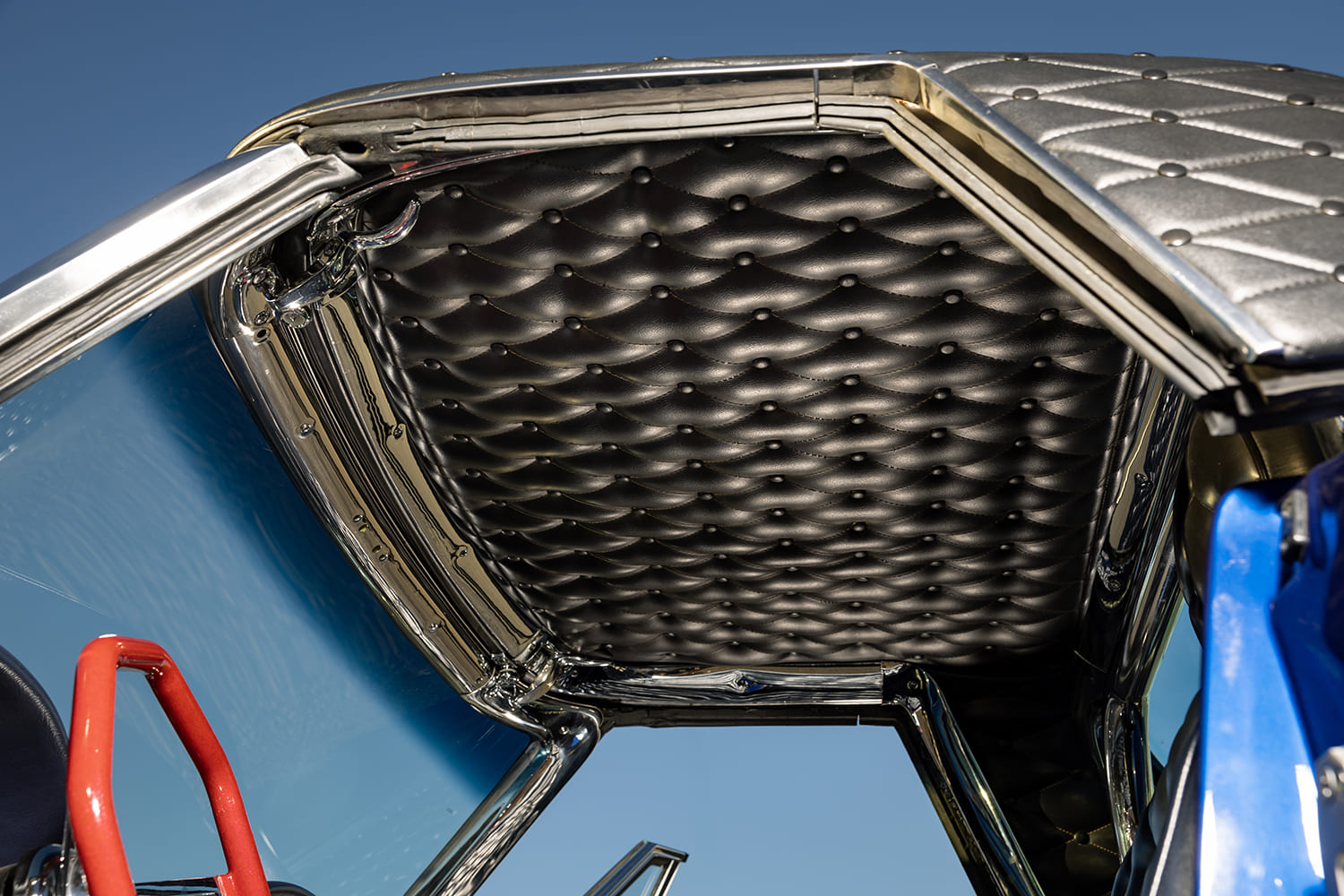 Upward interior view showing the black diamond-stitched headliner, chrome roll bar, and polished hardtop frame trim.