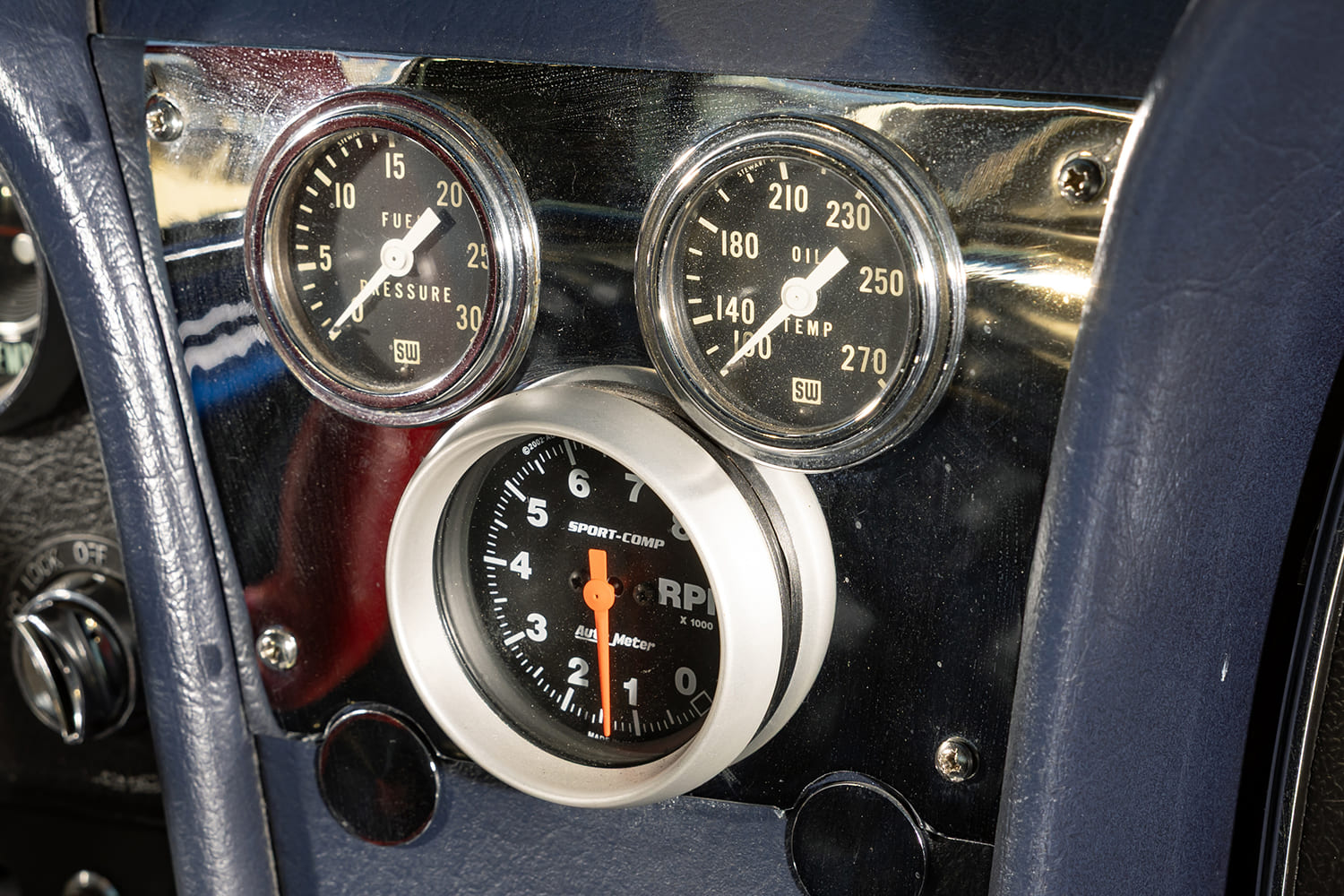 Close-up of the center console instrument pod featuring an Auto Meter Sport-Comp tachometer and Stewart-Warner fuel pressure and oil temperature gauges.