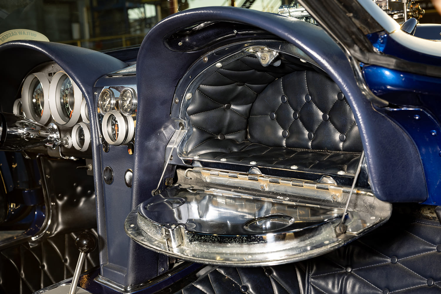 Open glovebox compartment revealing custom black button-tufted lining and chrome inner lid drink holder indents.