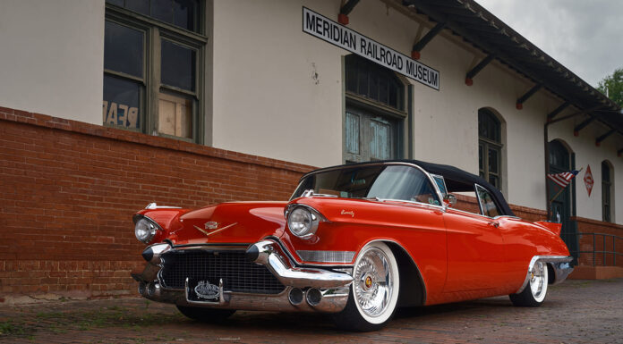 Low front three-quarter view showing the massive chrome front bumper, grille guards, Mike Curtis custom wheels, and Mike Goldman Customs license plate frame.
