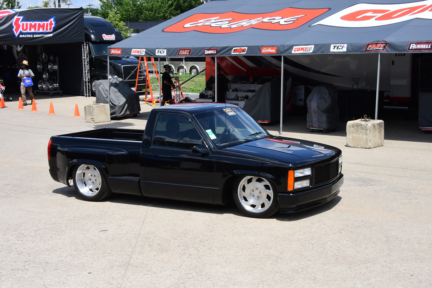 Low-slung gloss black 1990s Chevrolet C1500 stepside pickup on directional billet wheels parked outside the Summit Racing display tent.