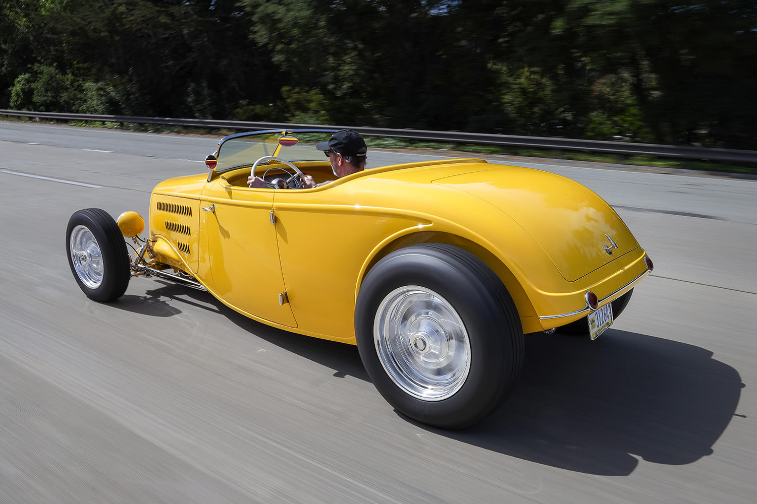 High-angle rear tracking shot capturing the yellow 1934 Ford roadster cruising down the highway.