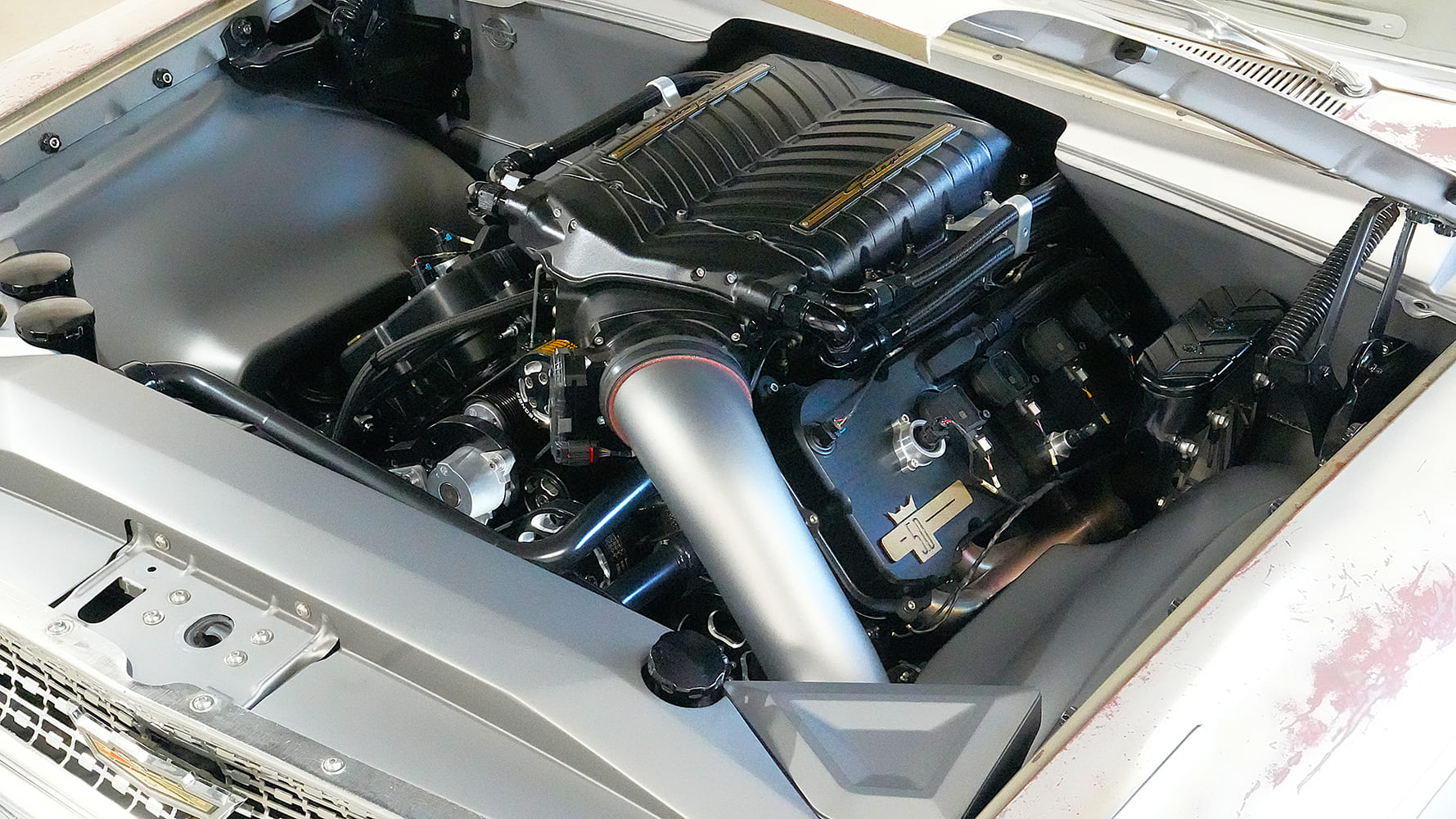 Top-down perspective of the 940-horsepower supercharged Coyote V8 nestled in a smoothed satin-finished engine bay with custom coil covers and fabricated intake plumbing.