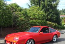 Front three-quarter view of John Gardiner's bright red 1975 Chevrolet Monza showing custom steel fender flares, American Racing wheels, and Corbeau seats parked curbside.