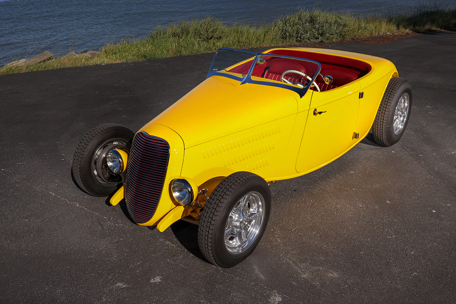 High-angle elevated view of the yellow 1934 Ford roadster showing the louvered hood sides, custom windshield, and red cockpit.