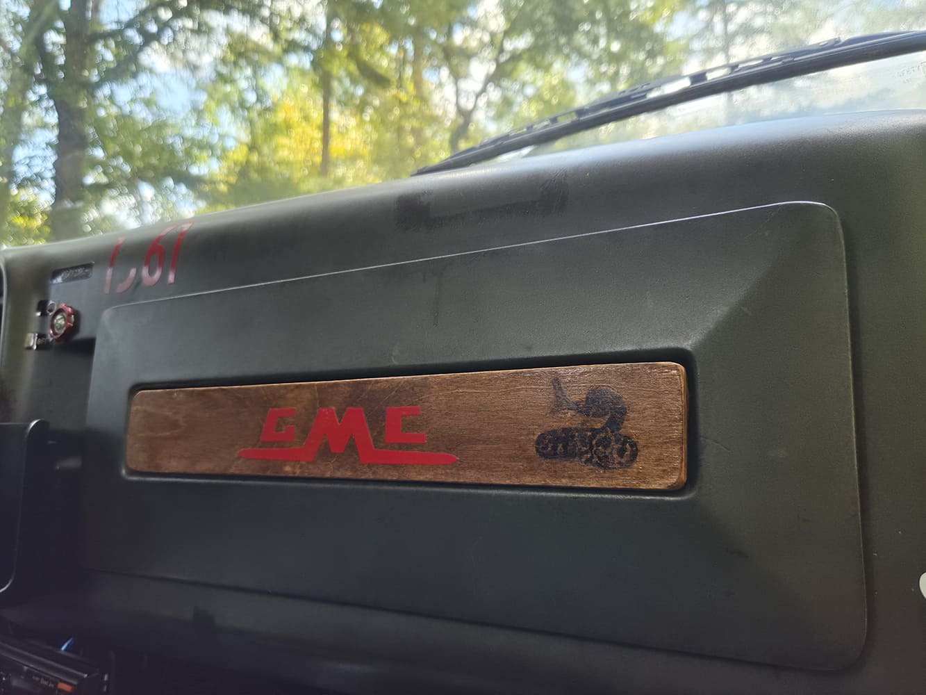 Detail of the glove box door on a 1967 GMC 7500 dashboard with custom wood inlay panel and red GMC lettering.