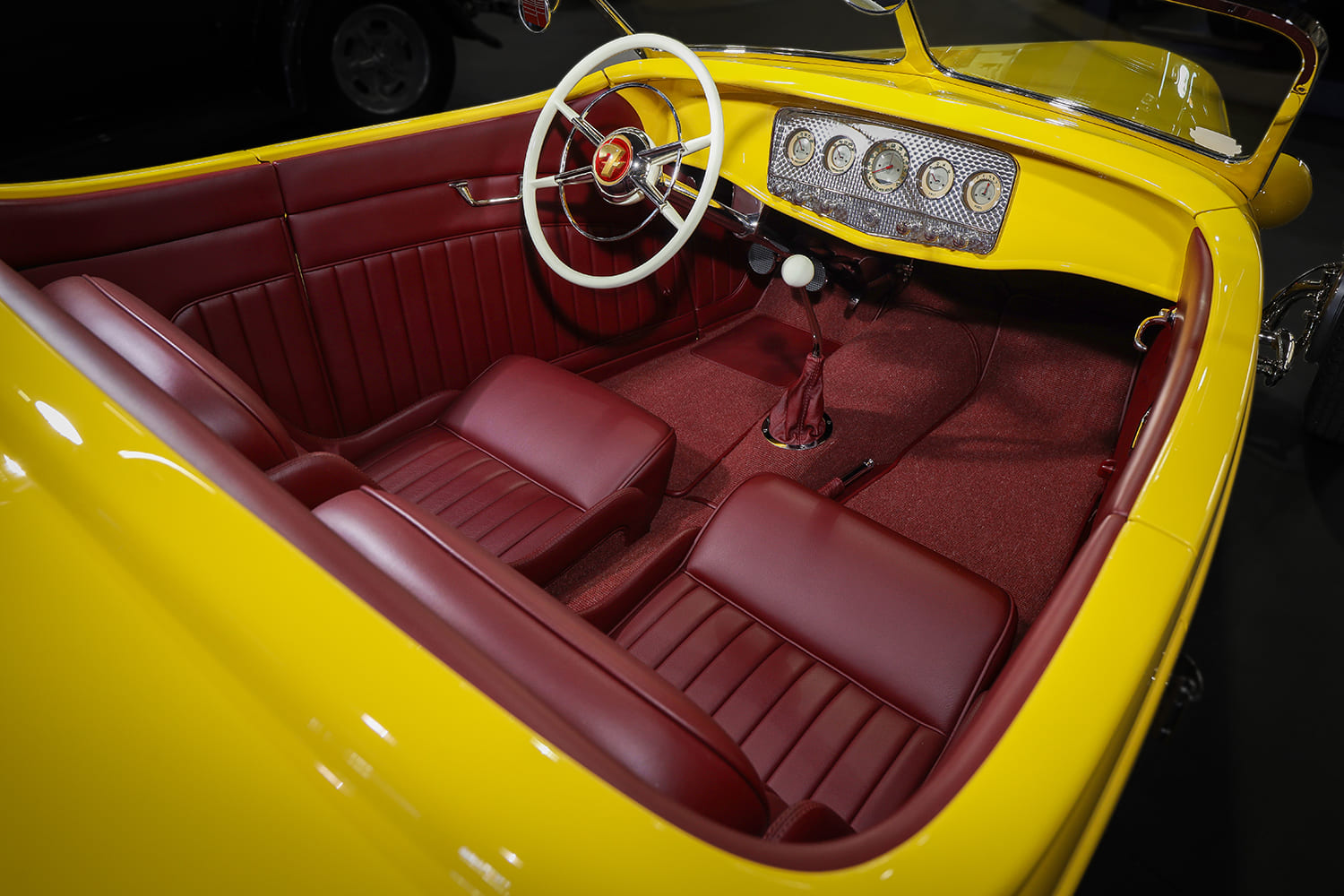 Wide high-angle view of the custom red leather bucket seats, matching carpet, white banjo steering wheel, and turned dash panel.