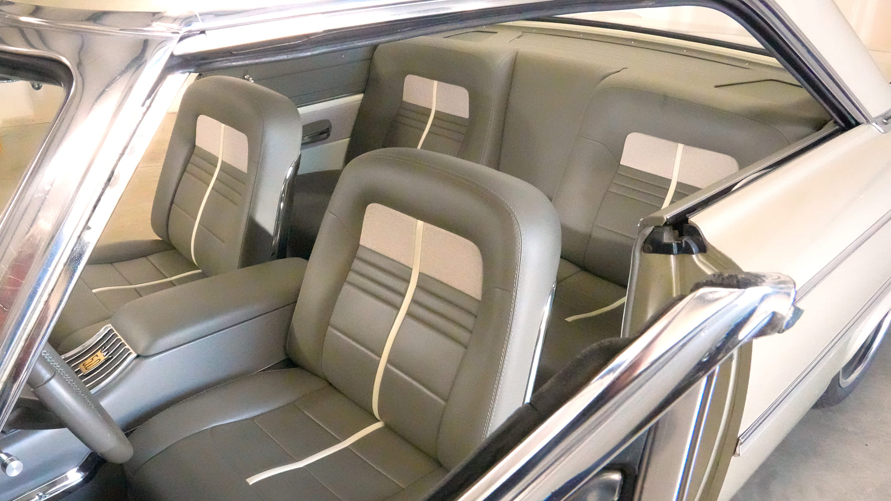 High three-quarter interior view looking across the driver-side door into the two-tone gray leather bucket seats and rear bench with white accent stripes