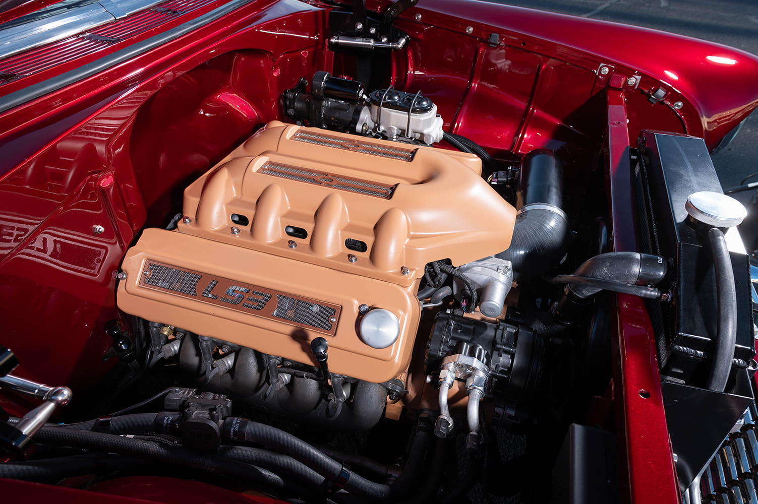 Close-up of the LS3 V8 engine highlighting custom caramel-tan engine covers with mesh inserts and LS3 lettering inside a gloss red smoothed bay.