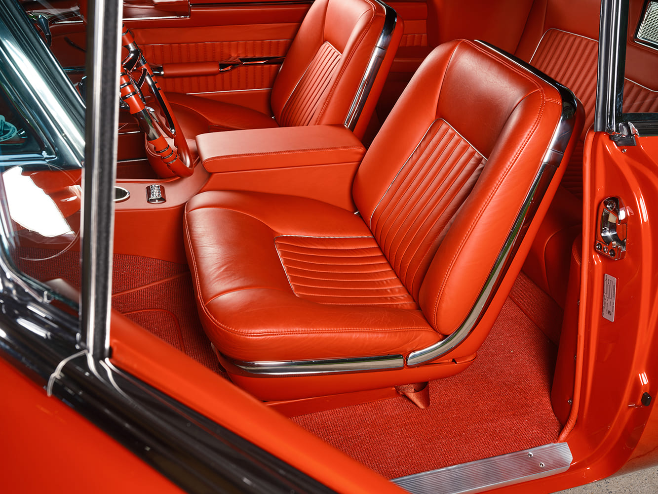 Wide view looking through the driver door at the pleated red leather bucket seats, chrome seat hinge trim, and red German square-weave carpeting.