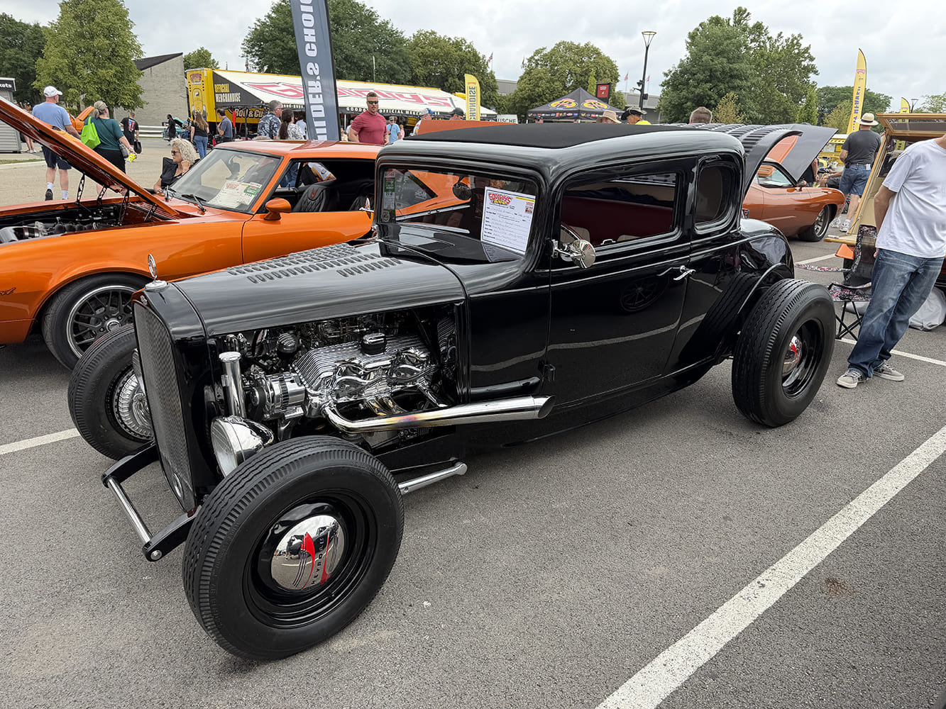 Front three-quarter angle of a traditional gloss black 1932 Ford coupe featuring chrome engine components, lakester headers, and black steel wheels with chrome caps.