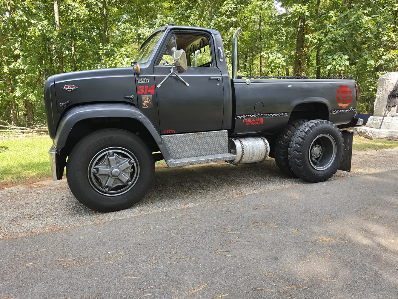 Driver side profile of a matte black 1967 GMC 7500 medium-duty custom truck with heavy-duty dually wheels and diamond-plate steps.