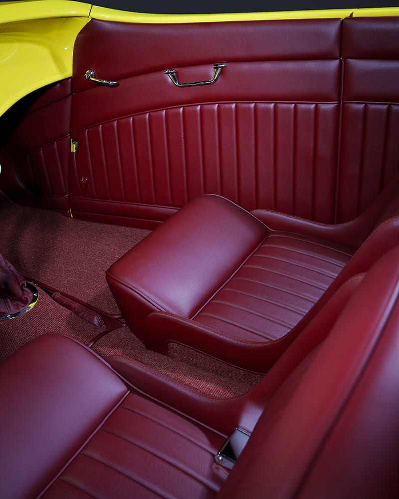 Interior passenger-side view highlighting the pleated red leather upholstery, chrome door release handle, and custom low-back bucket seat.
