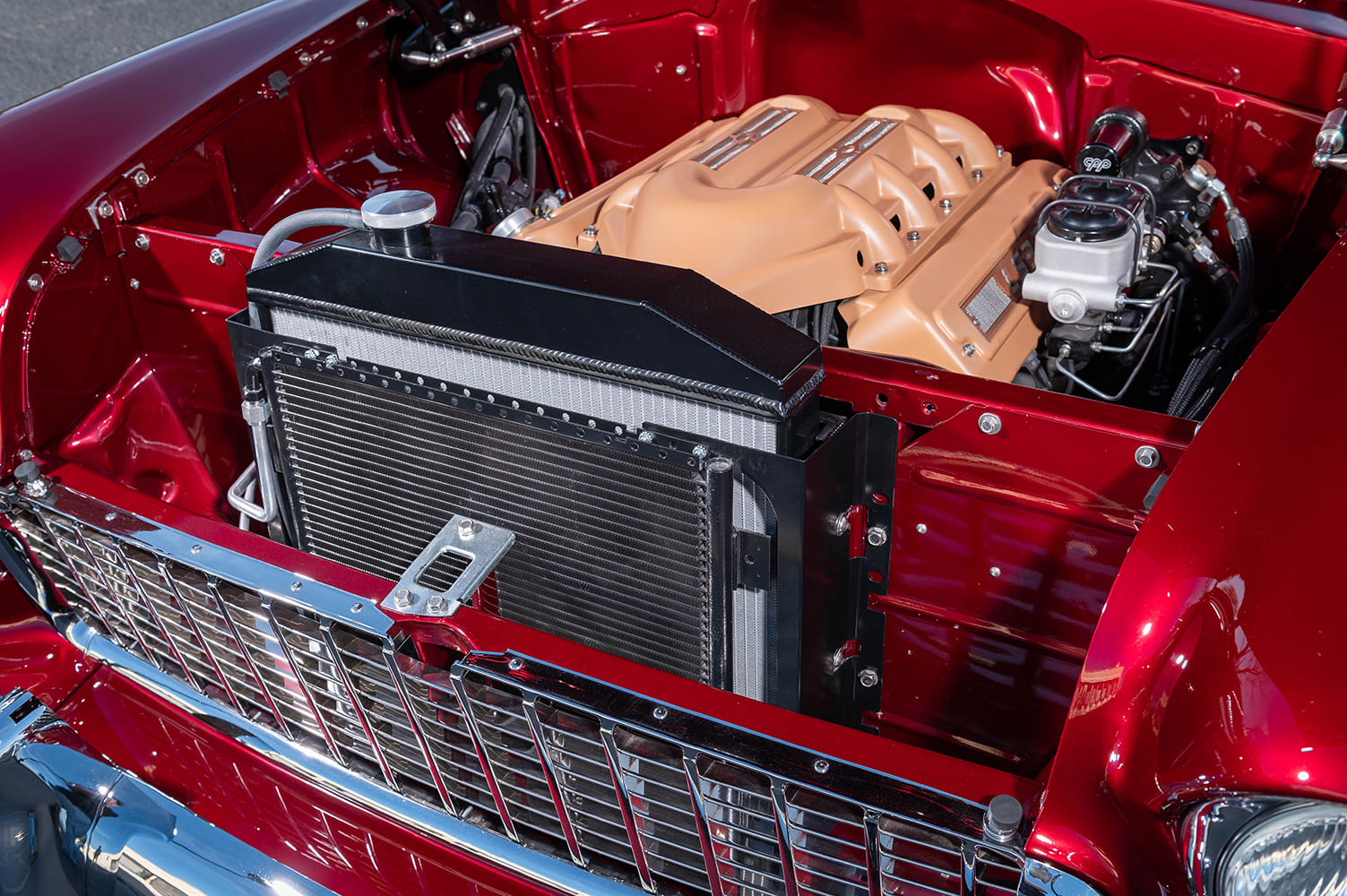 Front three-quarter engine compartment view showing the black powdercoated aluminum radiator support, cooling fins, and chrome egg-crate grille.